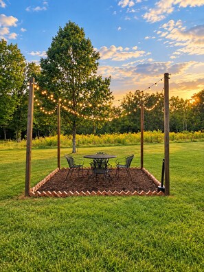 An outdoor seating area with a table and chairs, surrounded by a brick border, under string lights.