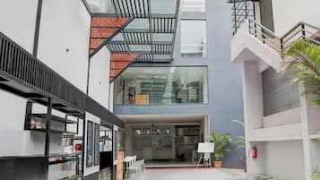 Un edificio moderno con fachada de vidrio, una escalera y un área de descanso con mesas y sillas.