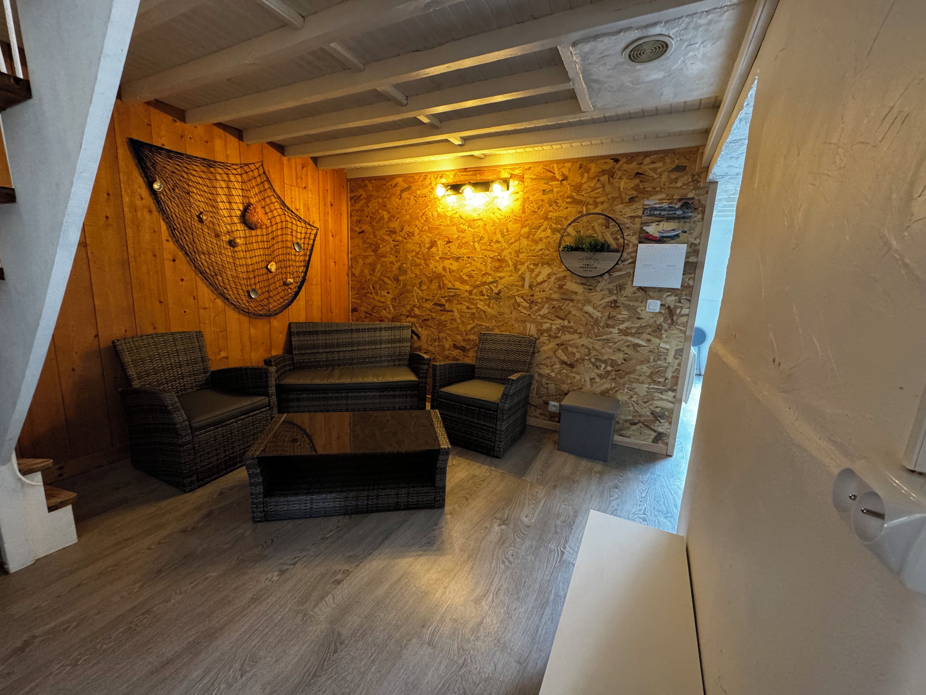 Een gezellige kamer met een houten plafond, een wandlamp en een rieten zithoek.