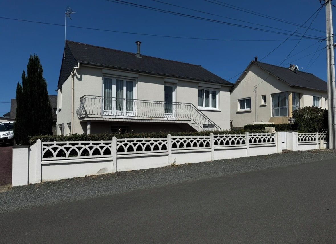 Une maison à deux étages avec un balcon, une allée et une clôture blanche.