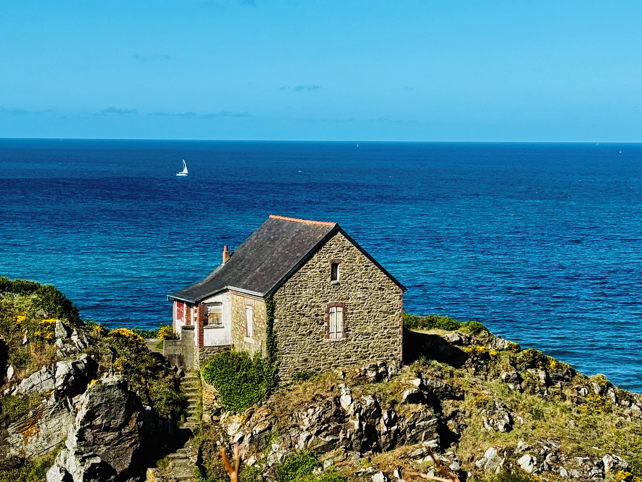 Une maison en pierre, dotée d’un toit à forte pente, située sur une côte rocheuse et offrant une vue sur la mer.