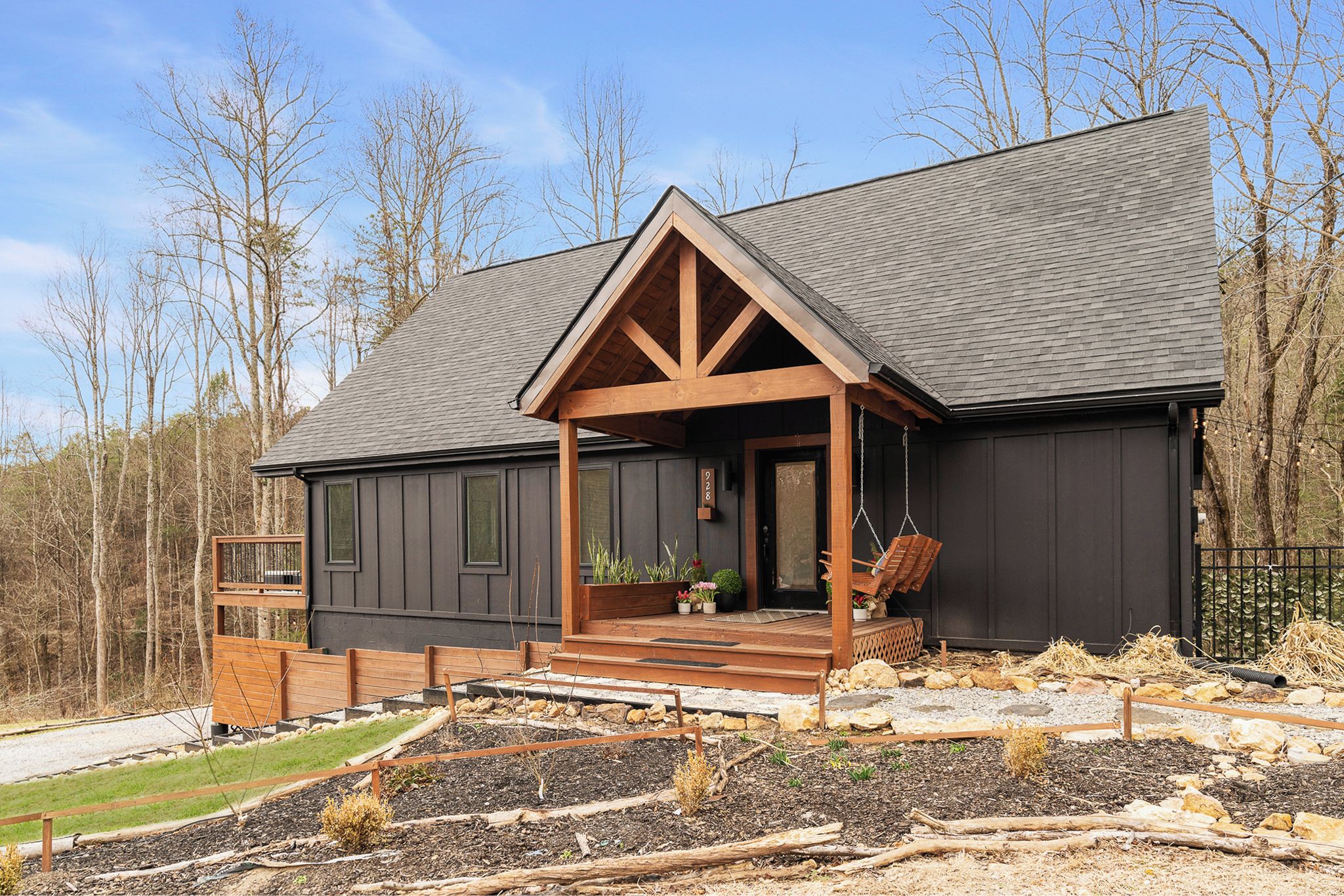 A modern house with a dark exterior, a wooden porch, and a stone pathway leading to the entrance.