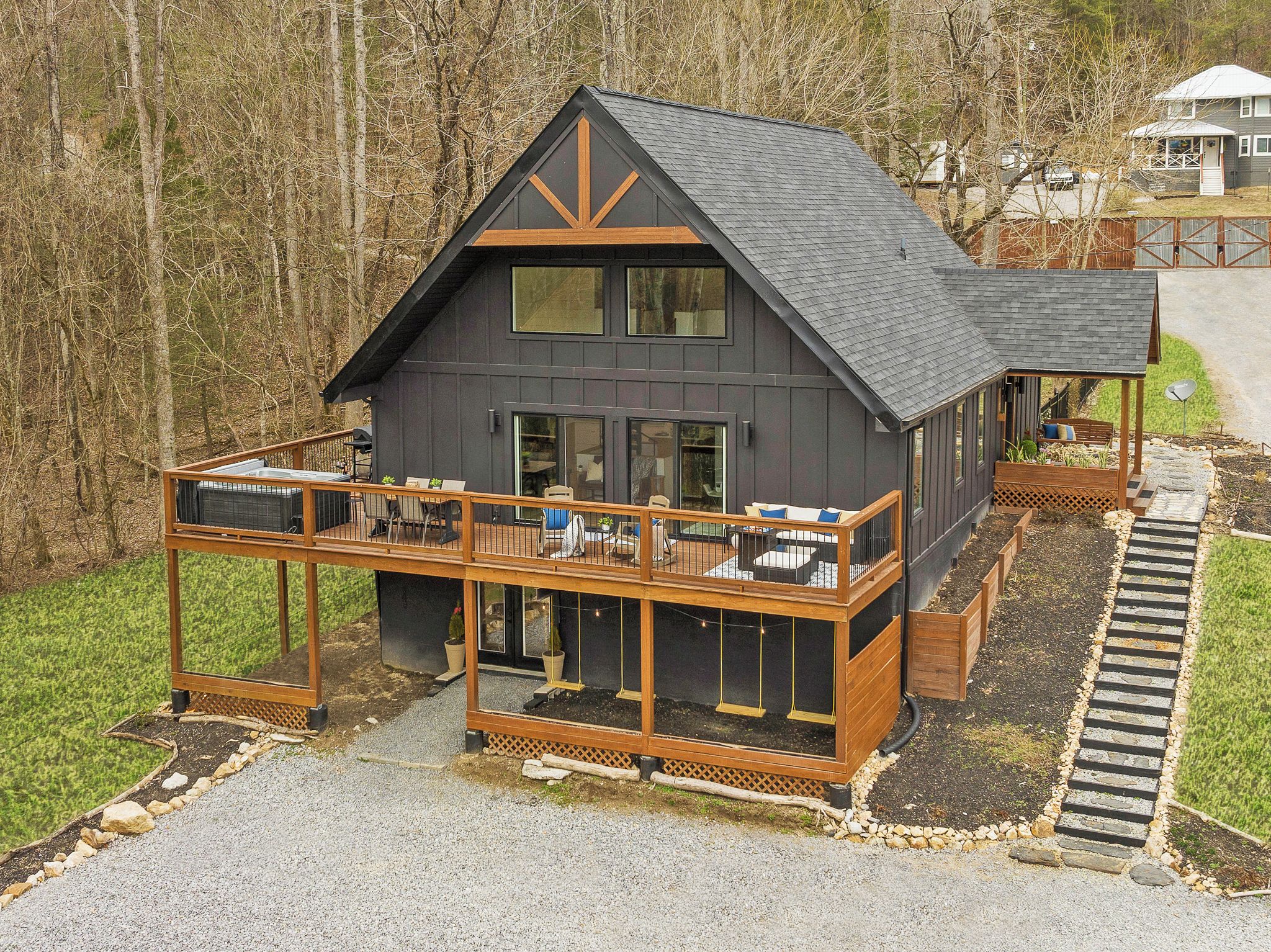 A modern two-story house with a balcony and a deck, surrounded by a forest.