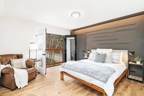 Een moderne slaapkamer met een groot bed, een leren fauteuil, een houten vloer en een balkon met een hekwerk.
