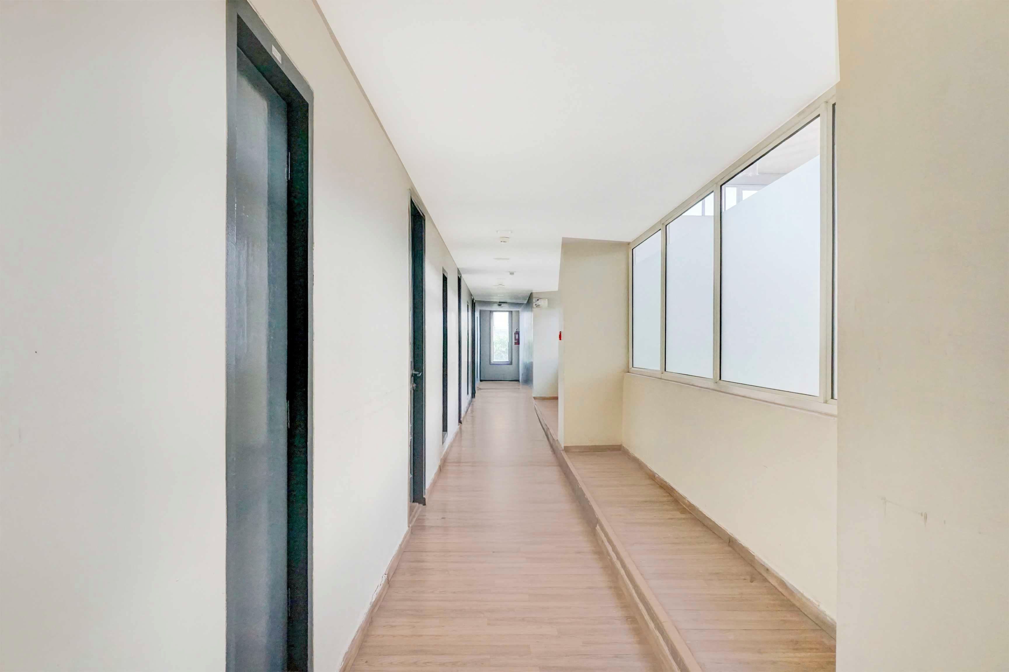 Un pasillo largo y estrecho con piso de madera y ventanas amplias en un lateral.