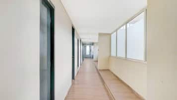 Un pasillo largo y estrecho con piso de madera y ventanas amplias en un lateral.