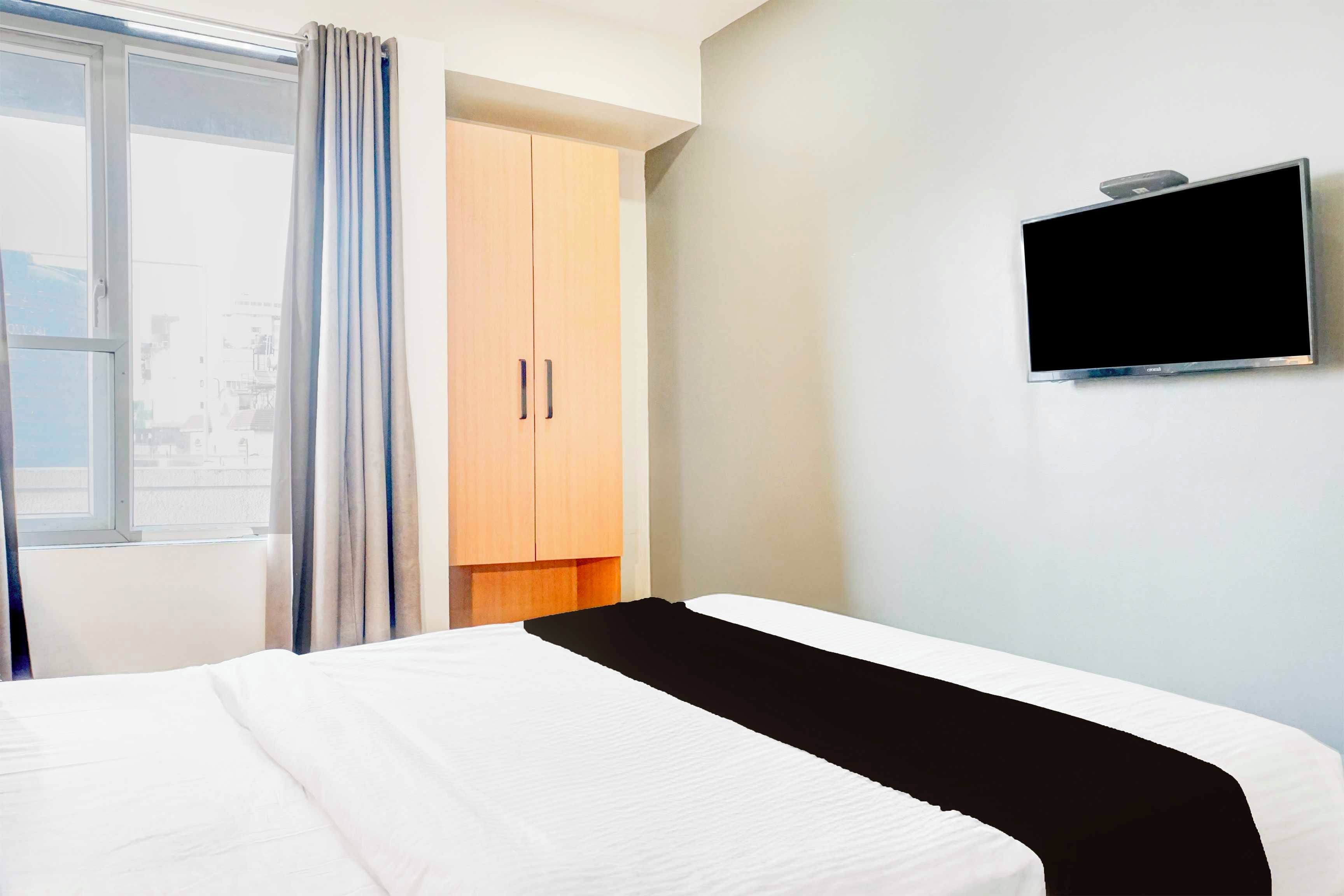 A hotel room with a bed, a TV mounted on the wall, and a window with curtains.