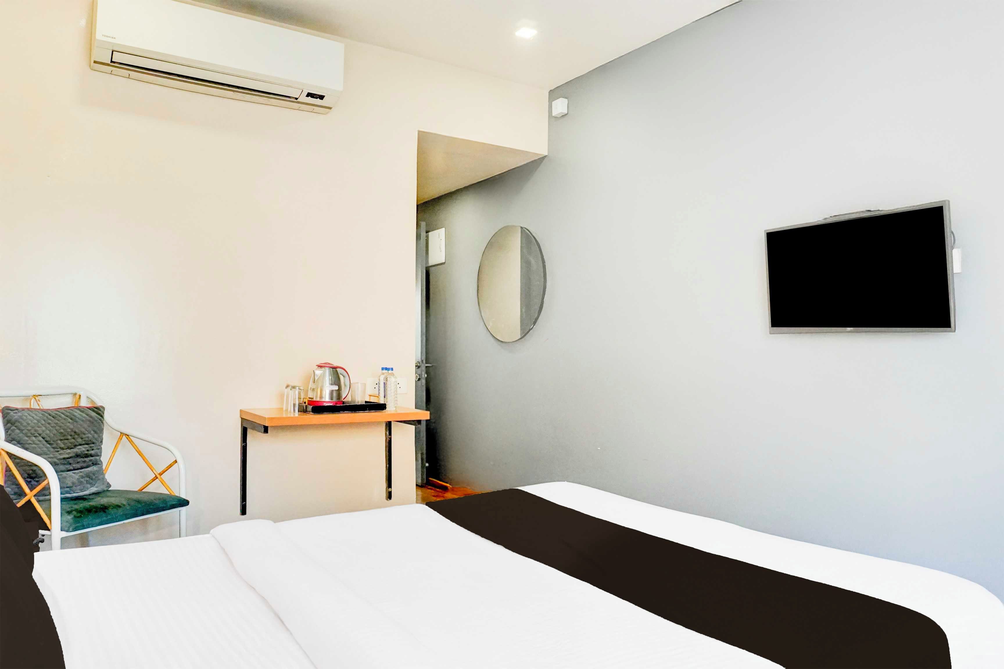 Habitación de hotel con cama, escritorio con tetera, una silla, televisión de pantalla plana y aire acondicionado.