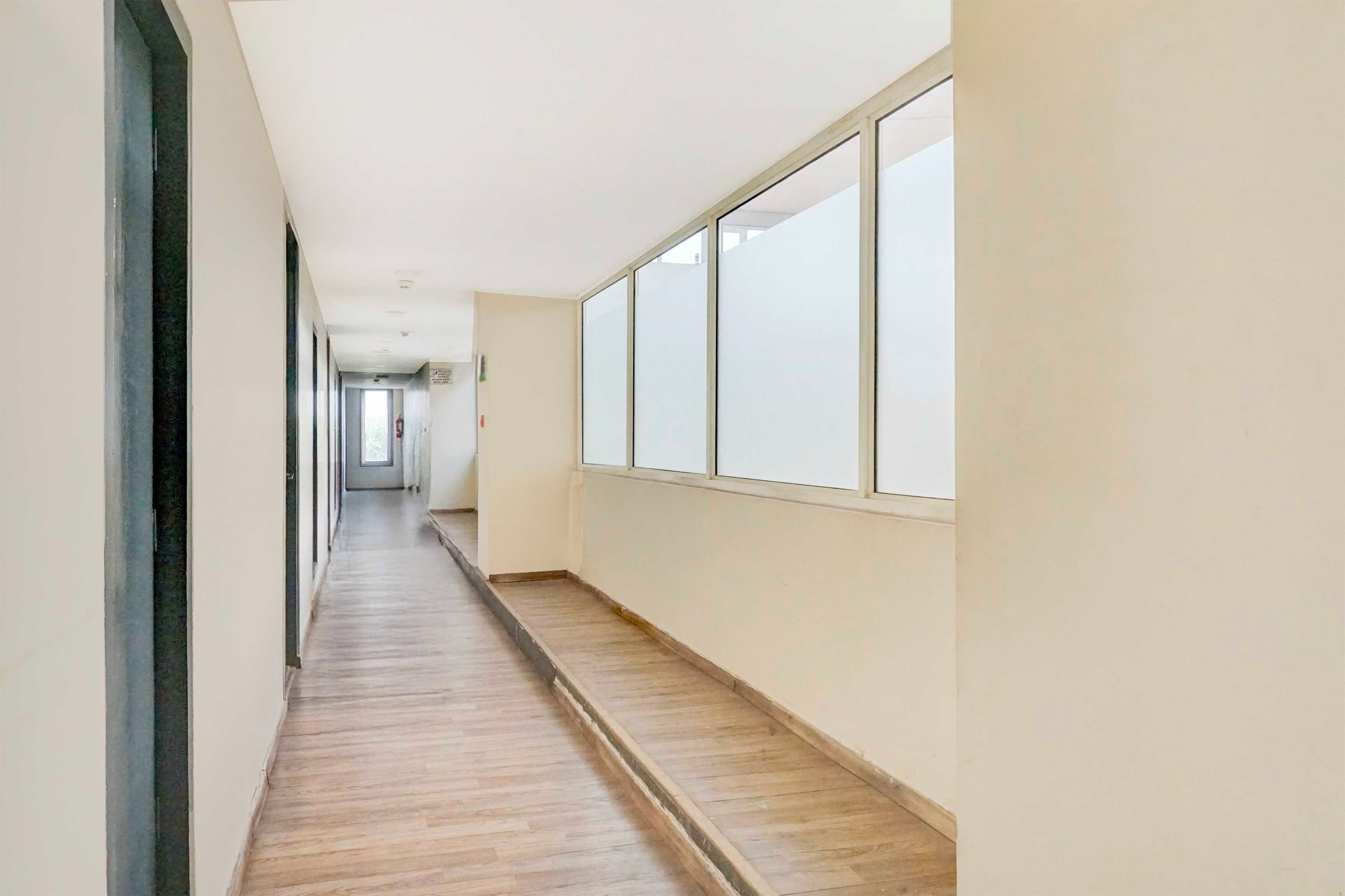 Un pasillo largo y estrecho con suelo de madera y ventanas amplias a un lado.