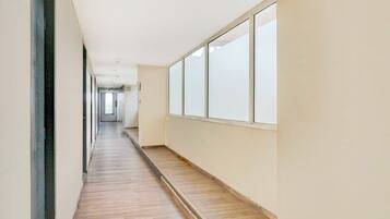 Un pasillo largo y estrecho con suelo de madera y ventanas amplias a un lado.