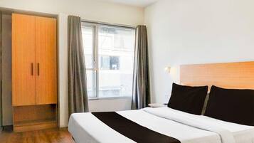 Een hotelkamer met een bed, een kledingkast, een raam met gordijnen en uitzicht op buiten.