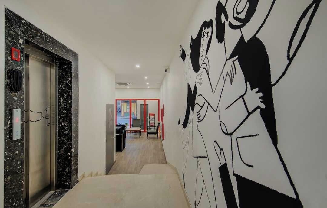 Un pasillo con pared de mármol, una puerta con marco rojo y un mural en la pared.