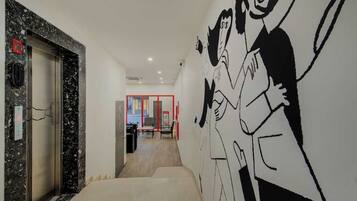 Un pasillo con pared de mármol, una puerta con marco rojo y un mural en la pared.