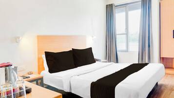 Een hotelkamer met een bed, een nachtkastje, een lamp, een raam met gordijnen en een houten garderobe.