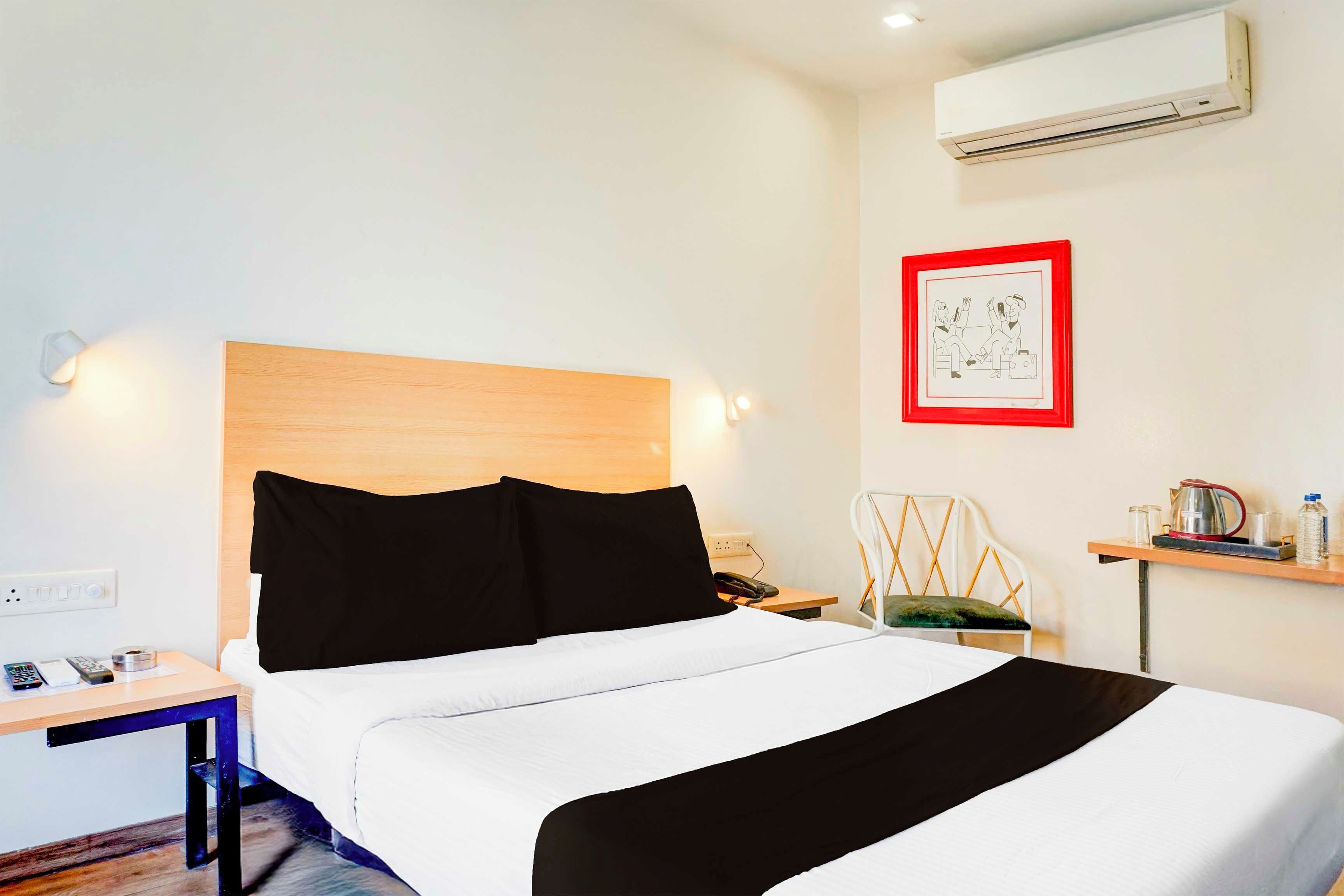 Habitación de hotel con cama, mesita de noche, silla, escritorio y un cuadro en la pared.