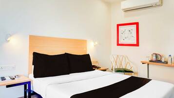 Habitación de hotel con cama, mesita de noche, silla, escritorio y un cuadro en la pared.
