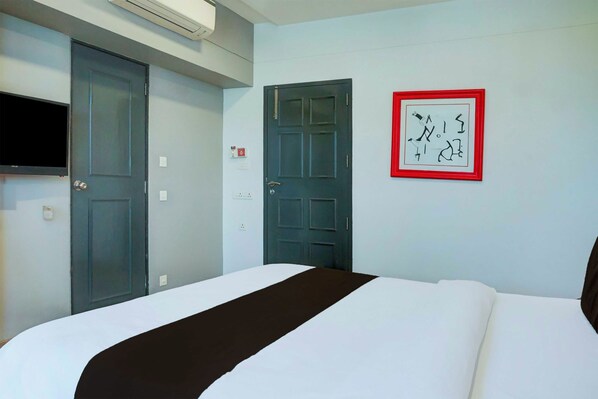 Quarto de hotel com uma cama, televisão, porta e uma obra de arte fixada na parede.