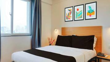 A hotel room with a bed, a nightstand, a phone, and a window with curtains. There are three framed artworks on the wall.