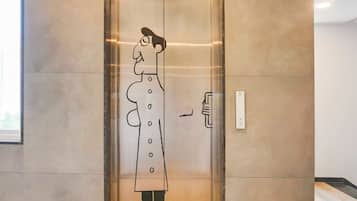 Un ascenseur dont une paroi est décorée d’une fresque représentant une personne portant un manteau.
