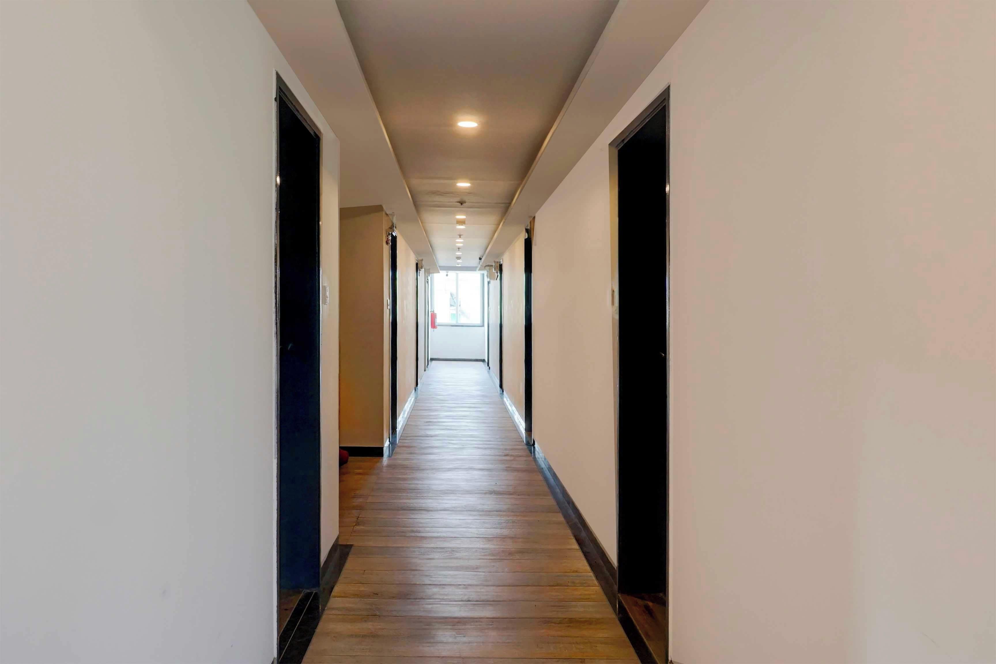 A long, narrow hallway with wooden flooring and white walls, leading to a bright room at the end.