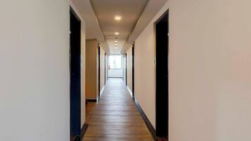 A long, narrow hallway with wooden flooring and white walls, leading to a bright room at the end.