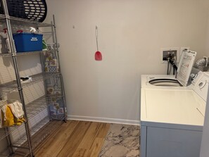 Uma área de lavanderia com máquina de lavar, prateleiras com produtos de limpeza e um esfregão.