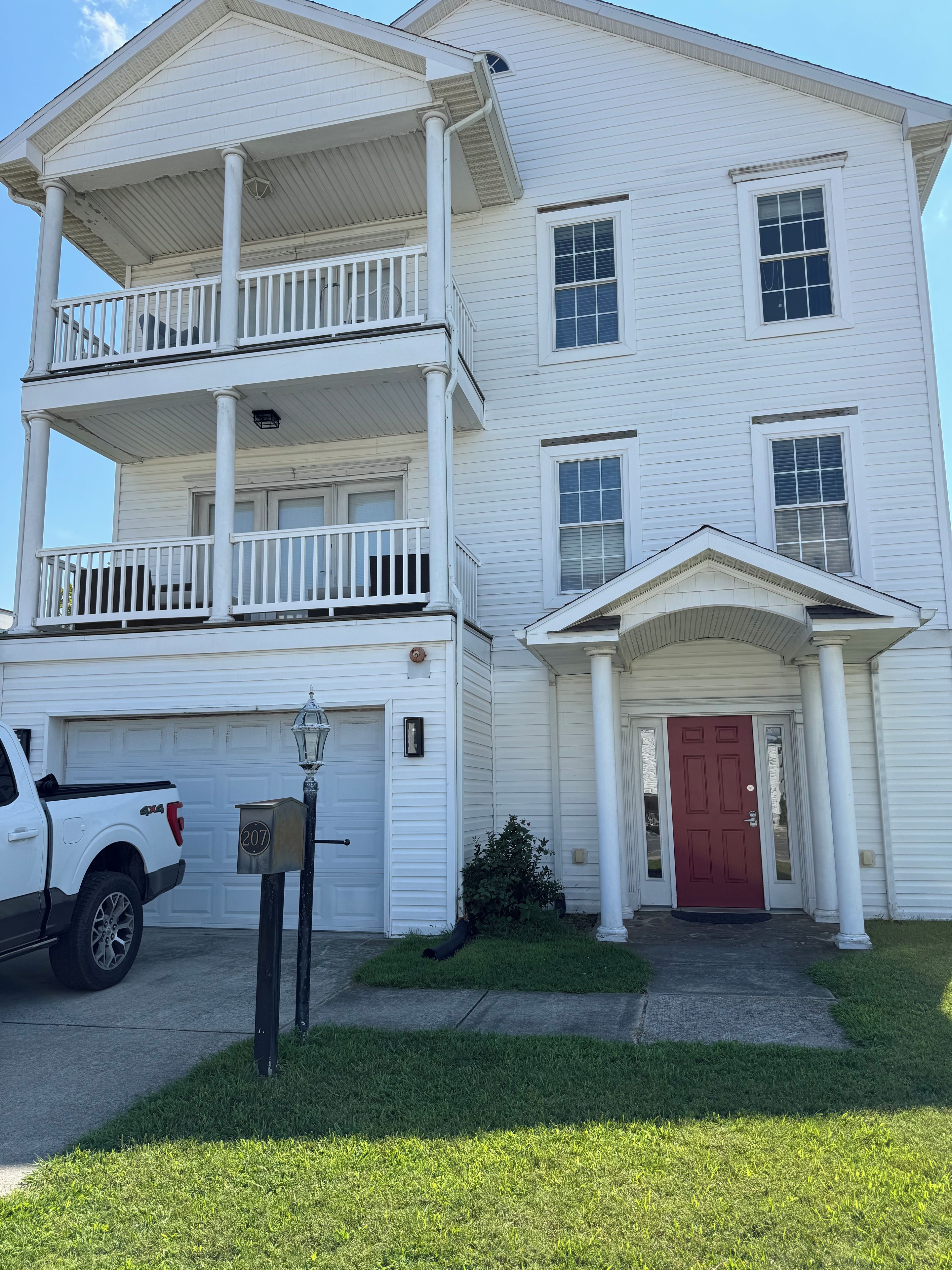 A two-story white building with a red door, a mailbox, and a parked white pickup truck.