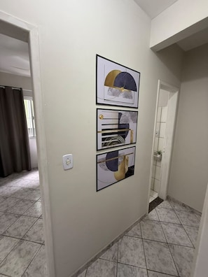 Un pasillo con suelo de baldosas, una puerta y tres cuadros abstractos en la pared.