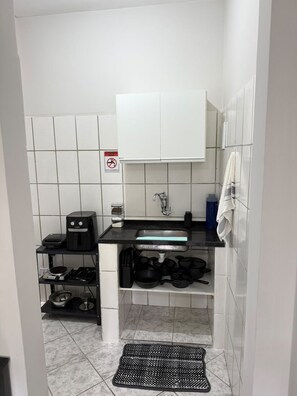 Cocina compacta con encimera negra, lavamanos blanco y cafetera.