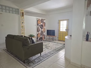 A living room with a sofa, a television, a patterned rug, and a door with a yellow gate. - Stylish Sanctuary: Mountain & Sea Views at Nya’s Place from Your Private Balcony (Tower Isle)
