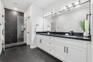 A modern bathroom with a large mirror, white cabinets, and a black countertop. - The NRG City Retreat (Houston)