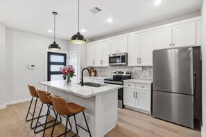 A modern kitchen with white cabinets, stainless steel appliances, and a central island with bar stools. - The NRG City Retreat (Houston)