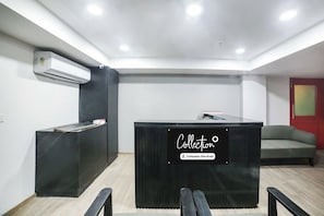 Un comptoir d’accueil avec une pancarte indiquant les services de l’entreprise, un comptoir noir, un canapé gris et un appareil de climatisation fixé au mur.