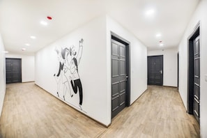 Un couloir orné d’une fresque murale, doté de plusieurs portes et d’un plancher en bois.