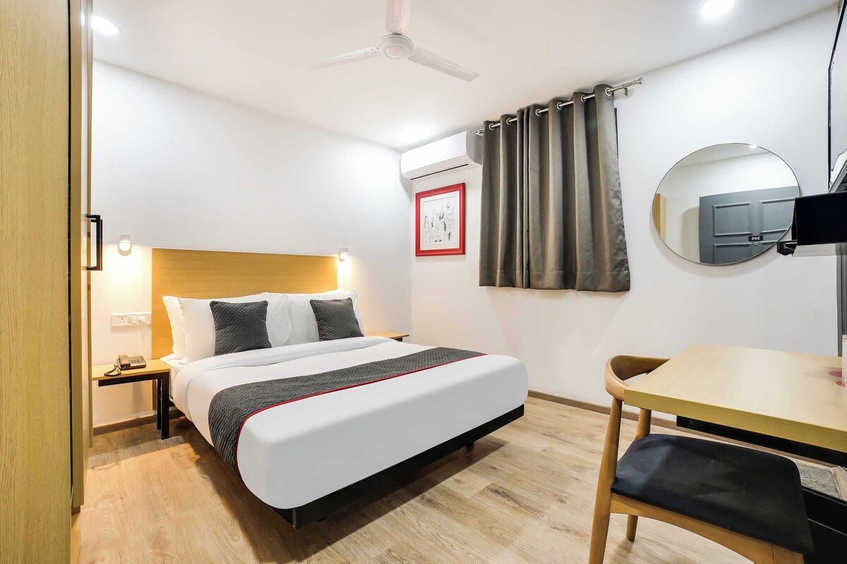 Een hotelkamer met een bed, nachtkastje, lamp, bureau, stoel en een plafondventilator.