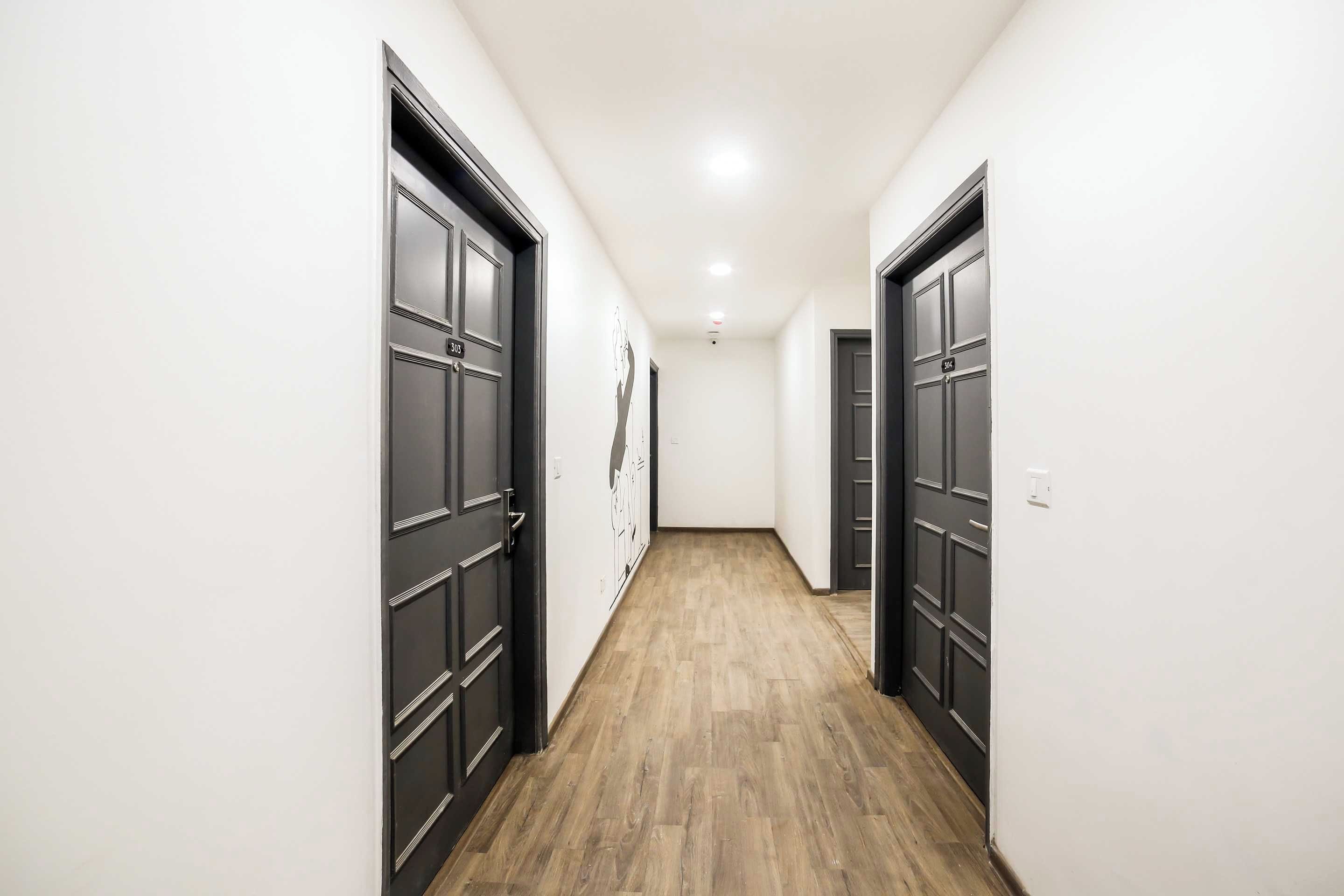 Un pasillo con puertas oscuras, paredes claras y suelo de madera.