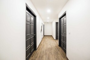Un pasillo con puertas oscuras, paredes claras y suelo de madera.