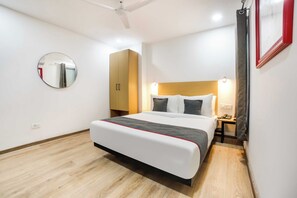 Een hotelkamer met een bed, nachtkastje, wandspiegel, garderobe en plafondventilator.