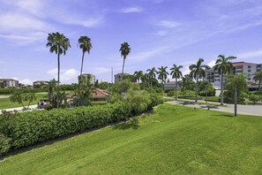 A well-maintained grassy area with palm trees and a building with a red roof. - NEW Golf Course View 2BR Condo | Isla Del Sol | St Pete (Isla Del Sol)
