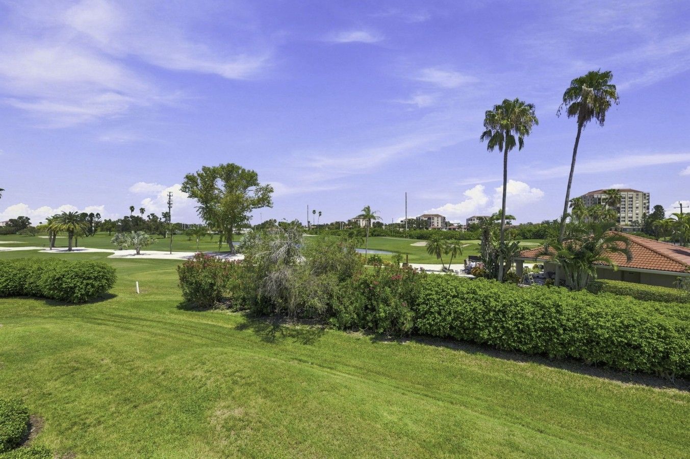Un terrain de golf bien entretenu, avec des pelouses impeccables, des palmiers et un ciel dégagé.