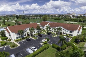 A multi-story hotel with a parking lot, surrounded by greenery and palm trees. - NEW Golf Course View 2BR Condo | Isla Del Sol | St Pete (Isla Del Sol)