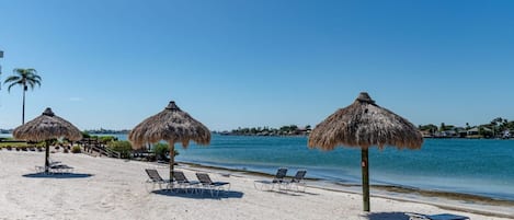 Una playa con sombrillas de paja y sillas de descanso.