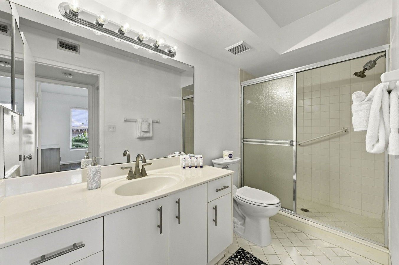 Un baño moderno con un espejo grande, un lavabo, un inodoro y una ducha con mampara de vidrio.