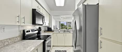 Una cocina moderna con armarios blancos, un refrigerador de acero inoxidable, un microondas y una estufa negra.