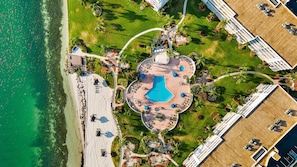 Luftaufnahme eines Resorts mit einem zentralen Pool, mehreren Gebäuden und einem Strandabschnitt.