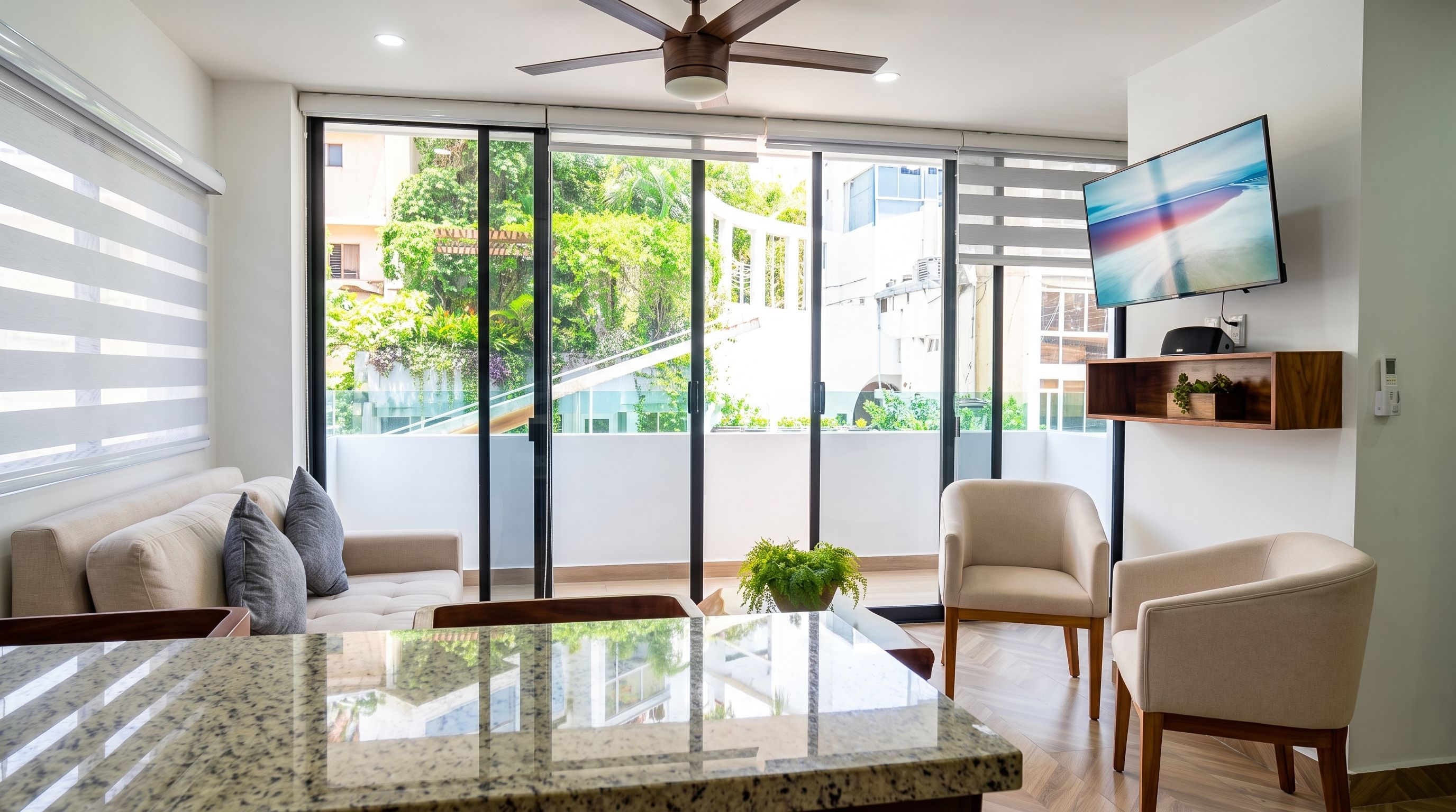Uma sala de estar moderna com uma grande porta de vidro deslizante, um ventilador de teto, uma TV de tela plana e um espaço de refeições com mesa de granito.