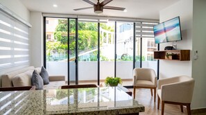 Uma sala de estar moderna com uma grande porta de vidro deslizante, um ventilador de teto, uma TV de tela plana e um espaço de refeições com mesa de granito.