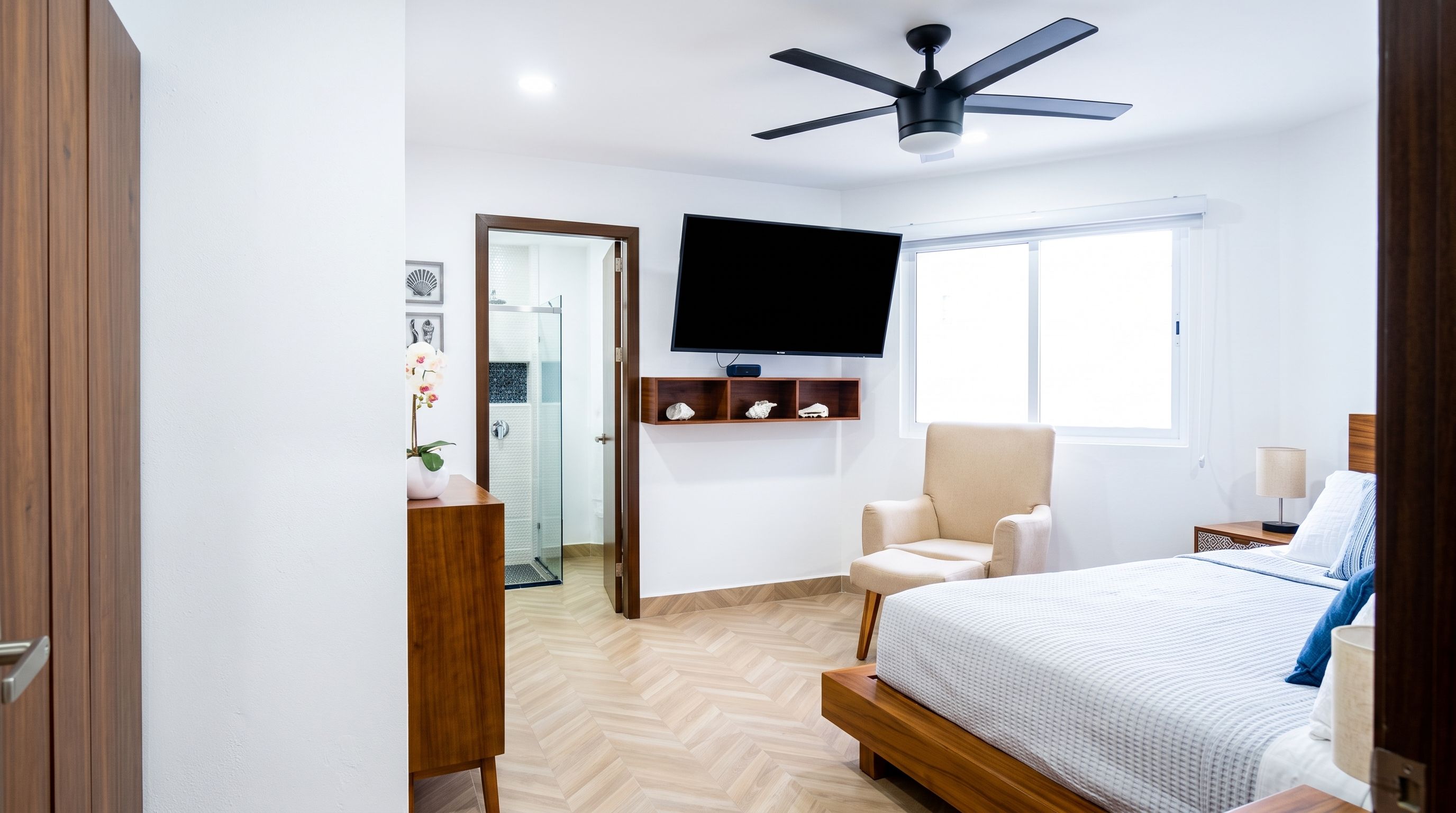 A bedroom with a bed, a chair, a television, and a ceiling fan.