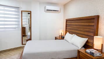 Habitación de hotel con cama, lámparas de noche, mesita de noche, aire acondicionado instalado en la pared y ventana con persianas.