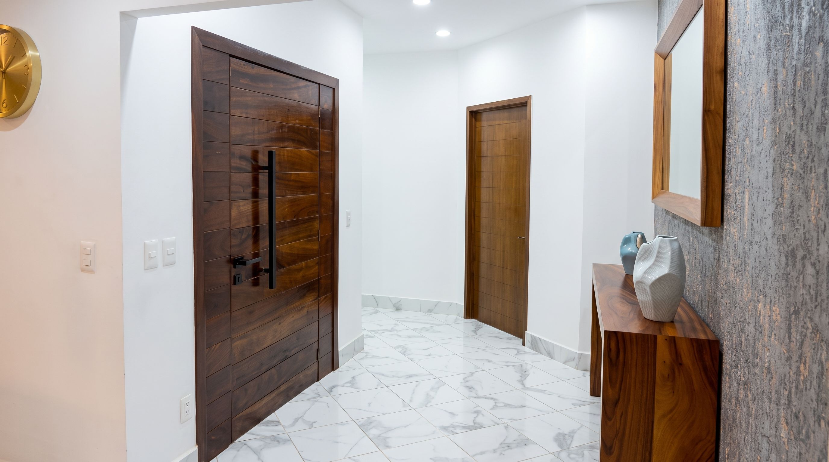 A hallway with a wooden door, a white wall, and a marble floor.